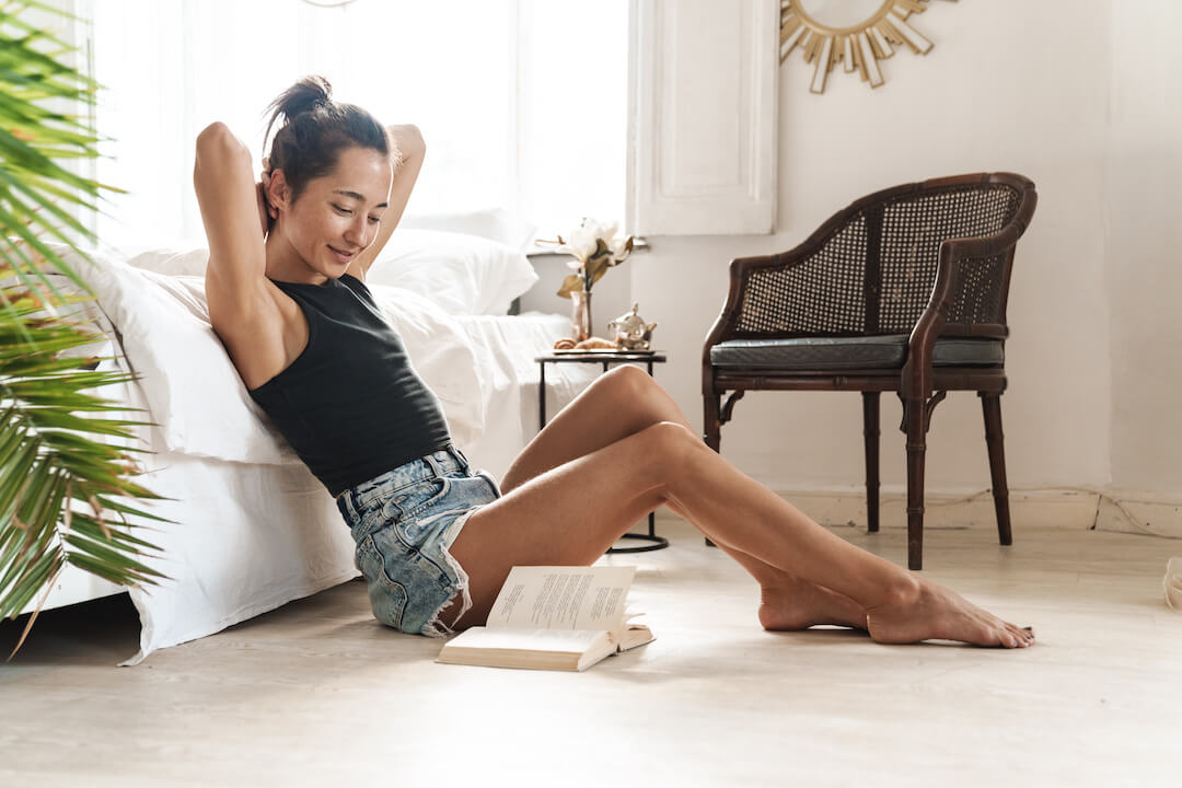 Femme assis au pied d'un lit lisant un livre.